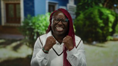 Parkta canlı örgüleri olan, gözlük takan ve rahat doğal ortamında heyecanını ifade eden bir kadın..