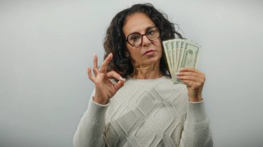Elinde dolar banknotları olan orta yaşlı bir kadın izole edilmiş beyaz bir geçmişe karşı iyi bir jest yapıyor. Finansal güven ve başarı tasvir ediyor..