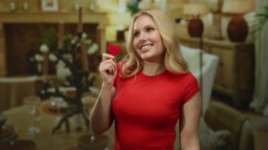 Kapalı alanda gülümseyen kırmızı kalpli bir kadın sıcak ışıklandırmalı ve bulanık arka planlı sıcak evde aşkı simgeliyor..