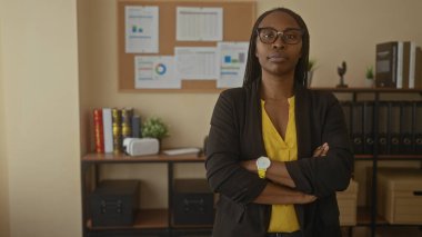 Ofiste kendine güvenen bir kadın, iş ortamını gösteren ciltler ve kitaplarla dolu bir kitaplığın önünde duran spor ceketi ayarlıyor.