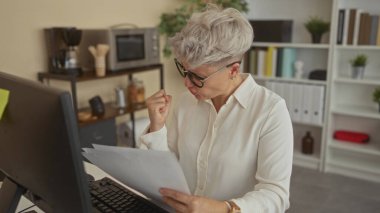 Bilgisayarın yanında bir yığın belge tutan ve ofis binasında yumruk pompası yapan bir kadın. Kariyer başarısı..