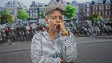 Şehir caddesinde bisiklet kiralama parkına karşı çenesinde dinlenen kısa gri saçlı kadın; tefekkür.