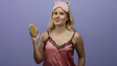 Pembe gece elbisesi giyen kadın, mor arka planda kendine güvenen bir vücut fırçası tutuyor, rahatlama ve güzellik rutini ifade ediyor..