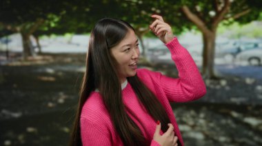 Pembe kazaklı bir kadın ağaçlarla dolu bir parkta neşeli bir şekilde gülüyor ve güneşli bir günün tadını çıkarıyor..