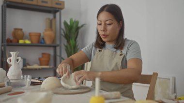 Çamur şekillendiren kadın, çömlek atölyesinde elleri ile çalışma alanı şekillendiren, önlüklü, aletli, seramik tencereli, sakin yaratıcılığı olan bir kadın..