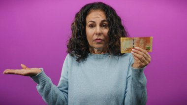 Orta yaşlı kadın, izole edilmiş mor bir geçmişe karşı kafa karıştırıcı bir ifadeyle Güney Afrika banknotunu elinde tutuyor. Bu da para yönetimi ile ilgili kafa karışıklığını simgeliyor..