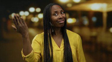 Gece bir şehir caddesinde, uzun saçlı, sarı tişörtlü, bulanık sokak lambalı bir şehir ortamında duygularını ifade eden bir kadın..