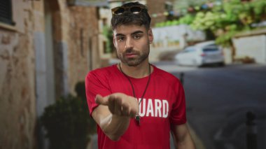 Kırmızı gömlekli bir cankurtaran eski şehir sokağında elinde taş binayla duruyor. Davetiye..