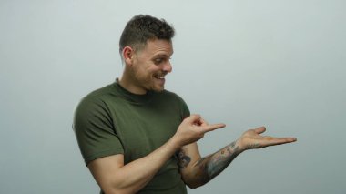 Beyaz arka planda avuçlarını gösteren dövmeleri olan genç İspanyol bir adam. Tarafsız bir duvarın üzerinden izole edilmiş tişört giyerken gülümsüyor ve cana yakın görünüyor..