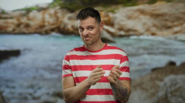 Çizgili gömlekli genç adam elleri ile bulanık bir deniz kenarı zeminine karşı, rahat ve çekici bir atmosfer taşıyor..