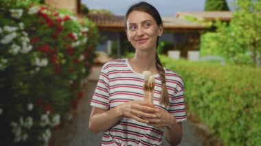 Bina girişinde iki eliyle boya fırçası tutan kadın, gözleri kapalı ve gülümsüyor; yaratıcı bir hobi.