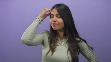 Mor arka planda duran bir kadın, alnına dokunurken düşünceli görünür. Düşüncelerini ve içyüzünü hafifçe gülümseyerek ifade eder..