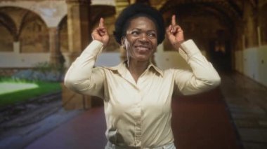 Kadınlar işaret parmaklarını yukarı kaldırıyor tarihi bir bina koridorunda ellerini gösteriyor ve gülümsüyor; sevinç kutlaması.