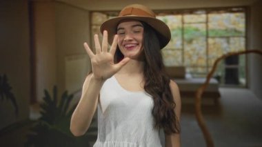 Hasır şapka ve kolsuz bluz giyen genç İspanyol kadın otel lobisinde beş parmağını gösteriyor..