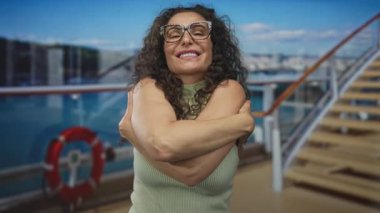 Kadın geniş gülüşlü, kıvırcık saçlı, gözlüklü ve çıplak kollu caddede sarılmak için kollarını uzatıyor..