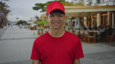 Restoran binasının dışında kırmızı t-shirt ve gözlüklü bir adam işaret ediyor..