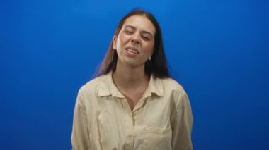 Stüdyoda elleri mavi arka planda kaldırılmış dillerini dışarı çıkaran genç bir kadın, neşeli yaramaz gençlik enerjisi..