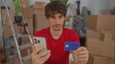 Yeni binanın içinde akıllı telefon ve kredi kartı taşıyan bir adam merdiven ve karton kutular taşıyor..