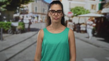 Yeşil kolsuz bluz giyen ve gözlüklü bir kadın şehir sokaklarında barış işaretleri gösterirken dilini uzatıyor..