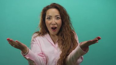 Genç beyaz bir kadın göğsüne yumruk indiriyor, elleri kırmızı tırnakları ve ağzı açık, uzun kıvırcık saçları var, solaryum duvarına karşı poz veriyor;.