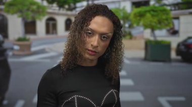 Şehir caddesindeki yaya geçidinde, park halindeki arabaların ve kavşağın yanındaki yeşil saksıların arasında kamerayı işaret eden ciddi ifadesi olan bir kadın..