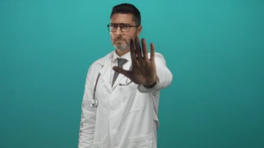 Steteskoplu beyaz önlüklü bir doktor, elinde avucuyla stüdyoda dur işareti yapıyor..