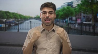 Kanal kenarında bej gömlekli genç İspanyol bir adam parmağıyla göğsünü işaret ediyor..