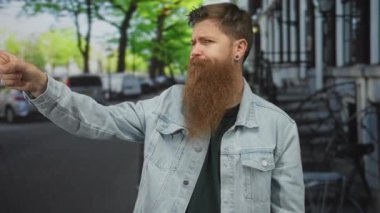 Kırmızı sakallı bir adam, park halindeki bisikletlerin yakınındaki, ağaçlık bir sokak üzerinde parmağını işaret ediyor..