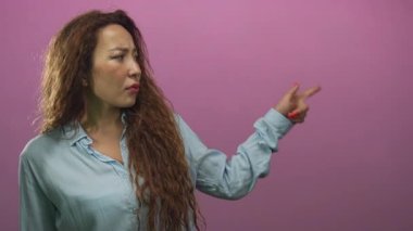 Pembe stüdyoda, kaşları çatık bir şekilde sol tarafa bakarken parmağıyla işaret eden ve kolunu kaldıran kadın tasvip etmiyor..