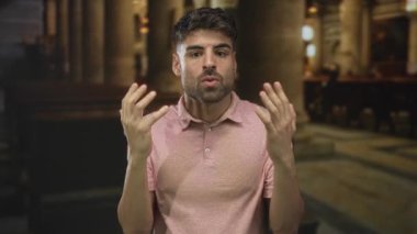 Genç İspanyol adam, kilisenin içinde, arkasında ahşap sıralar olan pembe gömlekli el kaldırıyor; sadakat inancına saygı..