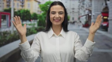Şehir merkezinde, sokak ortasında el kol hareketi yapan bir kadın neşeli bir ifade ve gün ışığında doğal güzellik, gençlik enerjisi ve özgüvenini simgeler..