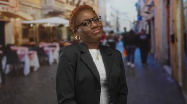 Gözlüklü ve altın küpeli bir kadın, restoranın teras masalarında gülümsüyor..