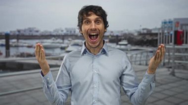 Açık mavi gömlekli genç adam yoğun limanda kolları geniş ve ağzı açık; heyecan dolu macera.