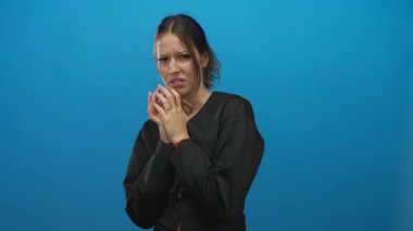 Genç İspanyol kadın ellerini sıkar ve yüzünü mavi stüdyoda gergin bir ifadeyle ve büzüşmüş dudaklarıyla kapatır..