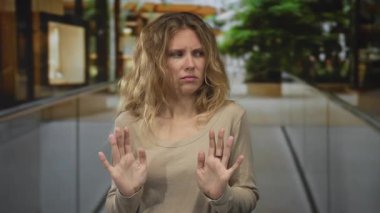 Kadın alışveriş merkezinin içinde engelleyici bir duruş sergiliyor. Sarışın genç bir denek iç mekanda endişeli ve somurtkan görünüyor..