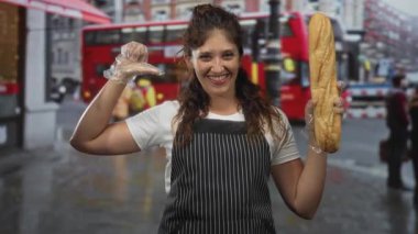 Eldivenli elle baget tutan ve kalabalık caddede çizgili önlükle gülümserken baş parmaklarını gösteren kadın, neşeli bir protesto..