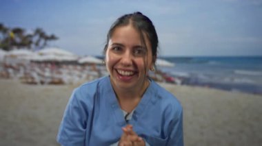 Mavi elbiseli genç İspanyol kadın sahilde güneşli bir günde gülüyor ve eğleniyor, palmiye ağaçları ve okyanus dalgalarıyla canlı bir sahil manzarası yaratıyor..