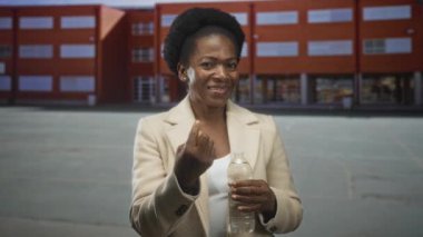 Tuğla okul binasının önünde elinde su şişesi tutan ve parmaklarıyla işaret eden kadın, hidrasyon toplumunu karşılıyor..