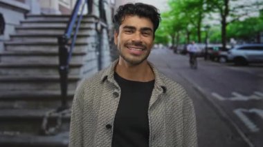 Ringbone ceketli gülümseyen İspanyol genç adam şehir sokaklarında çıplak yüzüyle dalgalanır..