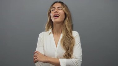 Sarışın, uzun saçlı ve kollarını kavuşturmuş bir kadın parlak stüdyo ortamında göz kırpıyor..