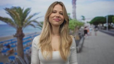 Sarışın kadın, iki eli deniz kenarında kaya boynuzları hareketi yapar; kaya eğlence gençliği enerjisi.