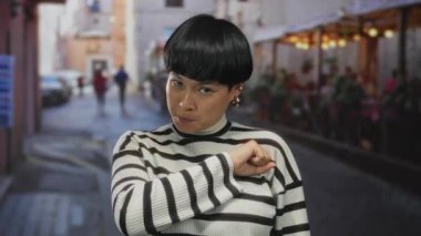 Restoran terasındaki genç Çinli kadın kardeşlik jesti yapıyor. Yumruğu göğsünde, açık havada çizgili süveter giyiyor..