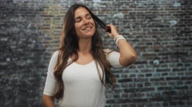 Bir kadın saçlara dokunuyor ve gülümsüyor. Stüdyoda, duvarları açık, beyaz, kendine güvenen bir kadın..