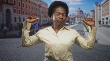 Kadın iki başparmağını da kaldırmış dirsekleriyle ve kaldırılmış bir kaldırım taşı sokağında kendine işaret ediyor. Kendine güvenen bir kimlik..