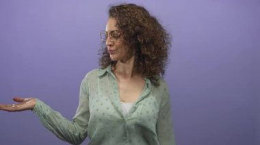 Avuçlarını kaldırıp mor stüdyoda elleri açık bir kadın. Nane rengi bluz ve yuvarlak gözlükler giyiyor..