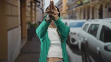 Elleri bağlı bir kadın yeşil hırka ve beyaz hasat bluzu giyerek bir şehir caddesinde öne doğru işaret ediyor; kararlılık odaklı dayanıklılık.