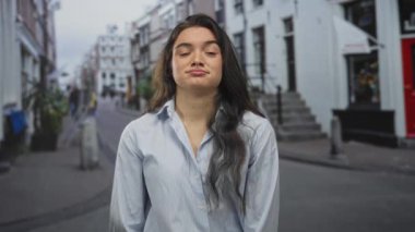 Dükkanların önündeki hareketli bir caddede tek gözüyle göz kırpan genç İspanyol kadın; kayıtsızlık..