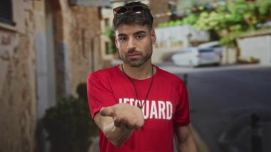 Kırmızı gömlekli bir cankurtaran eski şehir sokağında elinde taş binayla duruyor. Davetiye..