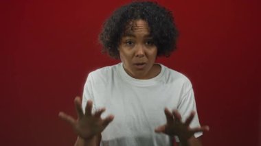 Beyaz tişört giyen Afro-Amerikalı genç bir kadın stüdyo ortamında kırmızı arka planda çıplak elle hareket ederken görülüyor..