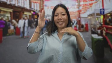 Elleri havada bir kadın kalabalık bir şehir pazarında gün ışığında kameraya gülümsüyor..